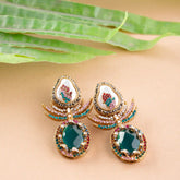 Ornate earrings with gemstones on a beige surface with green leaves.