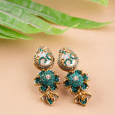 Pair of gold and green earrings on a beige surface