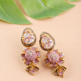 Pair of ornate earrings with pink floral designs on a beige surface