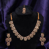 Gold necklace set with matching earrings on a black stand against a purple background