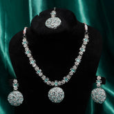 Jewelry set with necklace, earrings, and tikka on a black stand against a green satin background