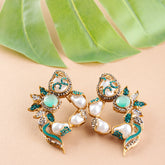 Pair of ornate earrings with pearls and turquoise stones on a beige background with green leaves.