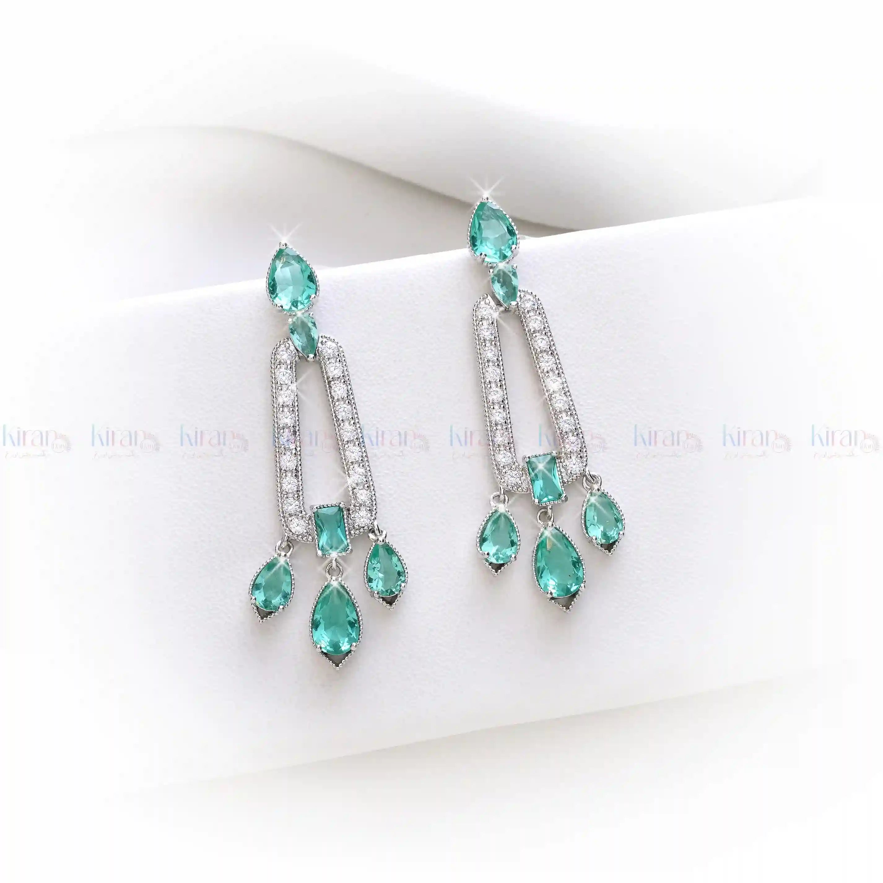 Teal chandelier earrings on a white surface with "KiranDan" branding.