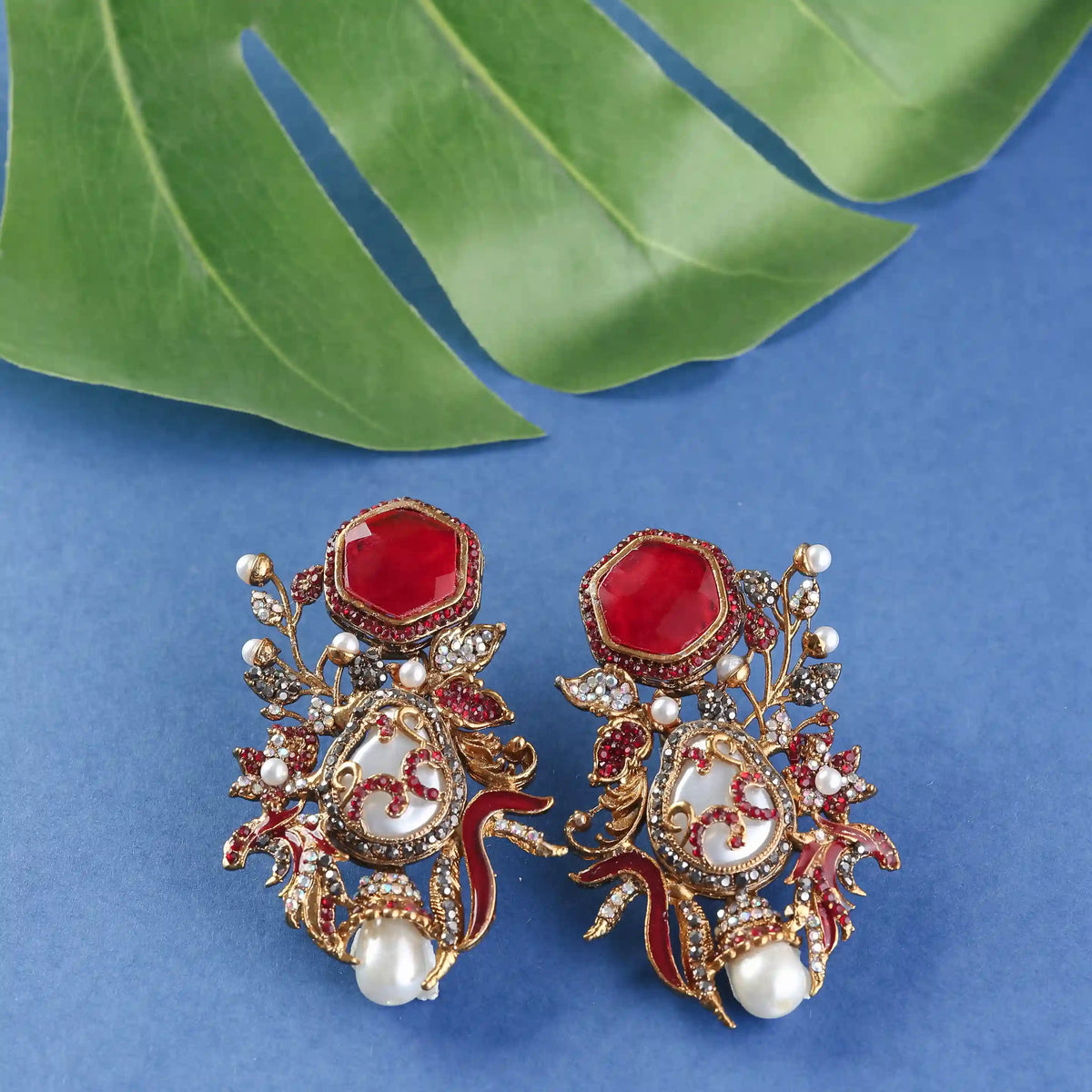 Ornate earrings with red and gold details on a blue background