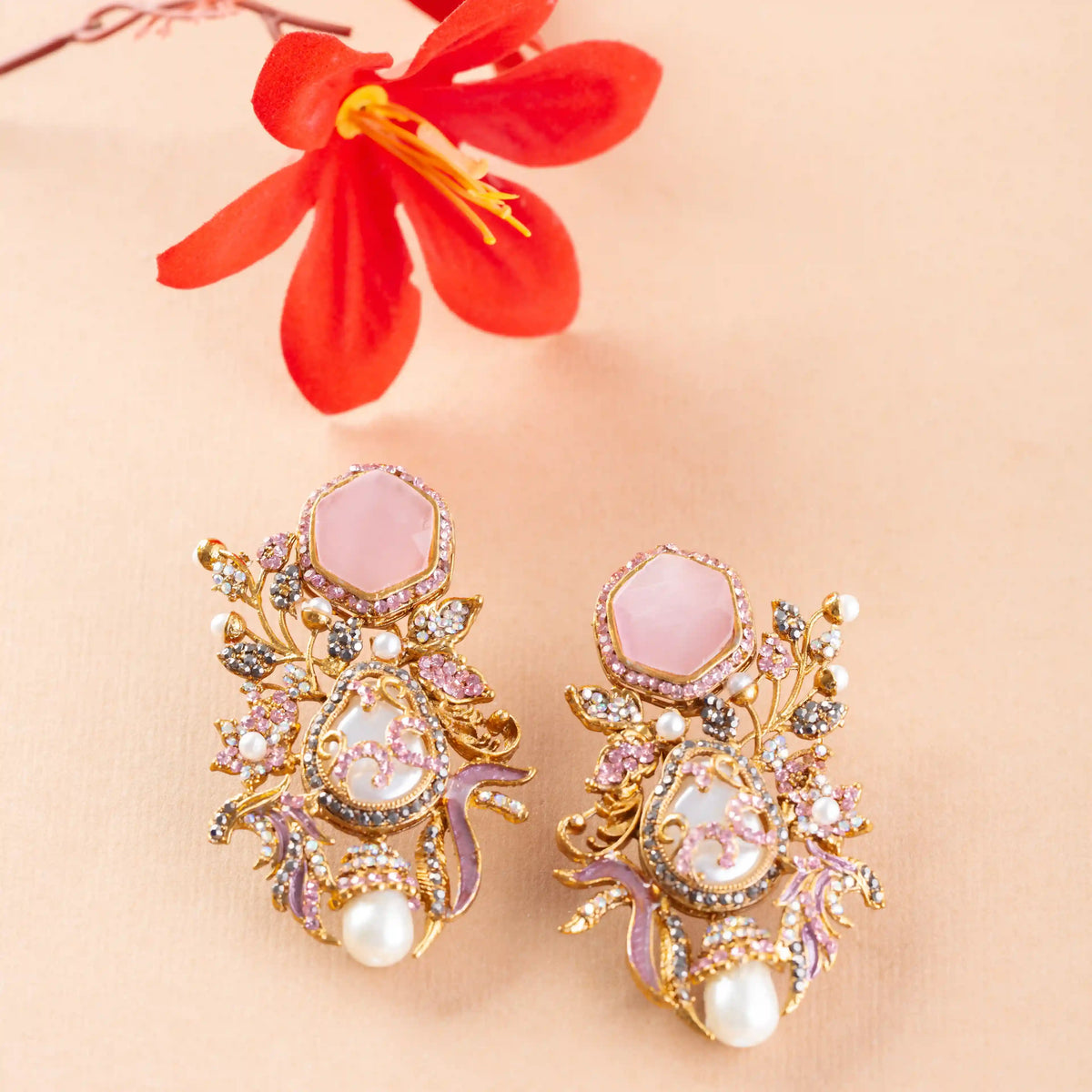 earrings with pink stones and pearls on a beige background with a red flower.