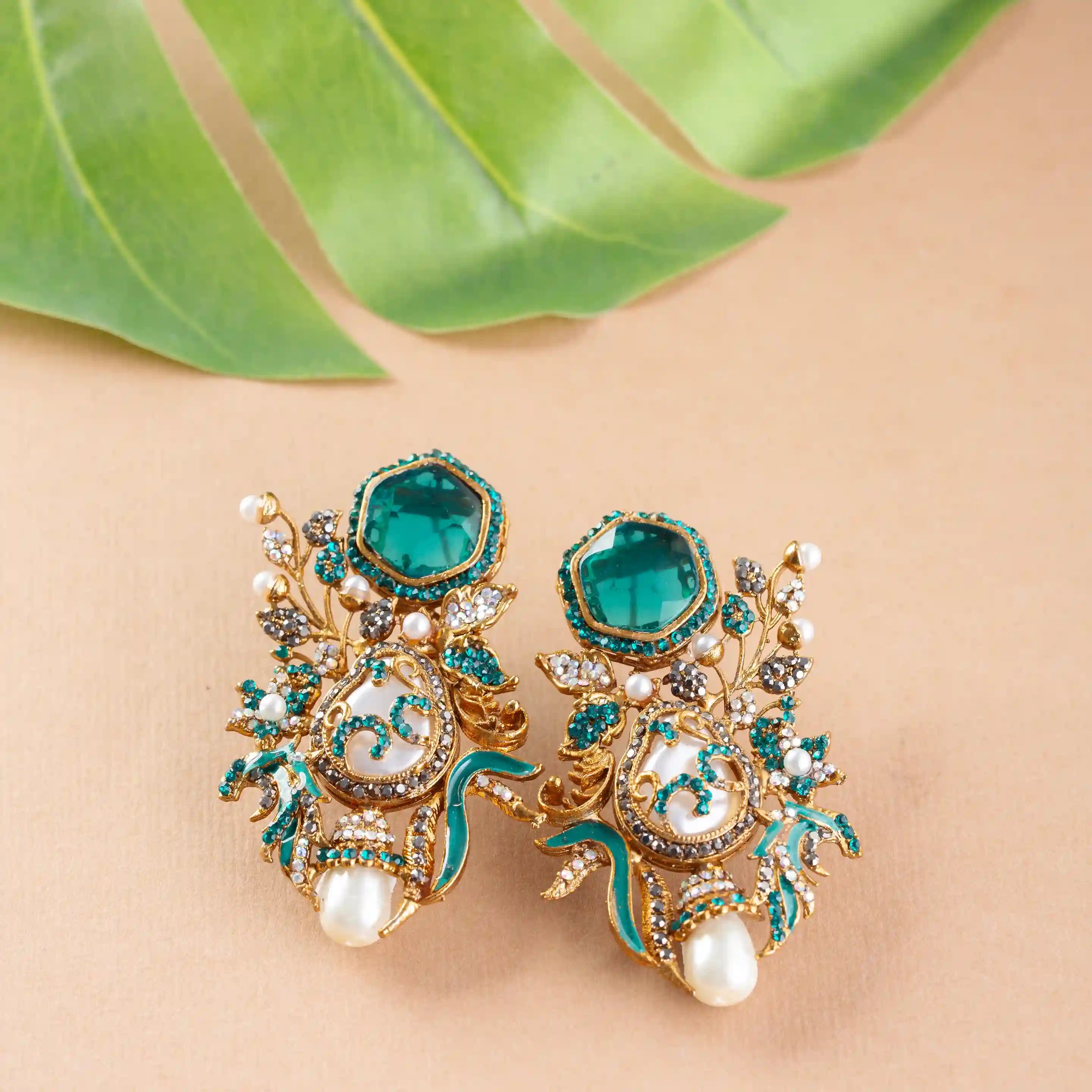 Ornate earrings with green gemstones and gold accents on a beige background