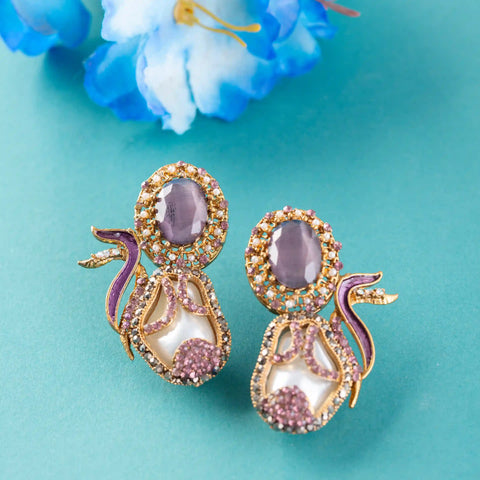 Ornate earrings with purple and gold details on a teal background
