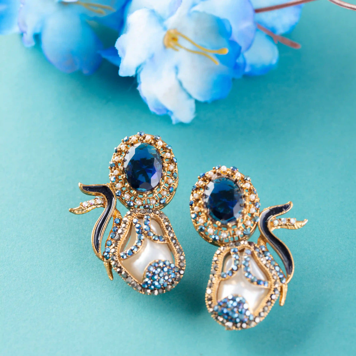 Gold and blue earrings on a turquoise background with blue flowers.