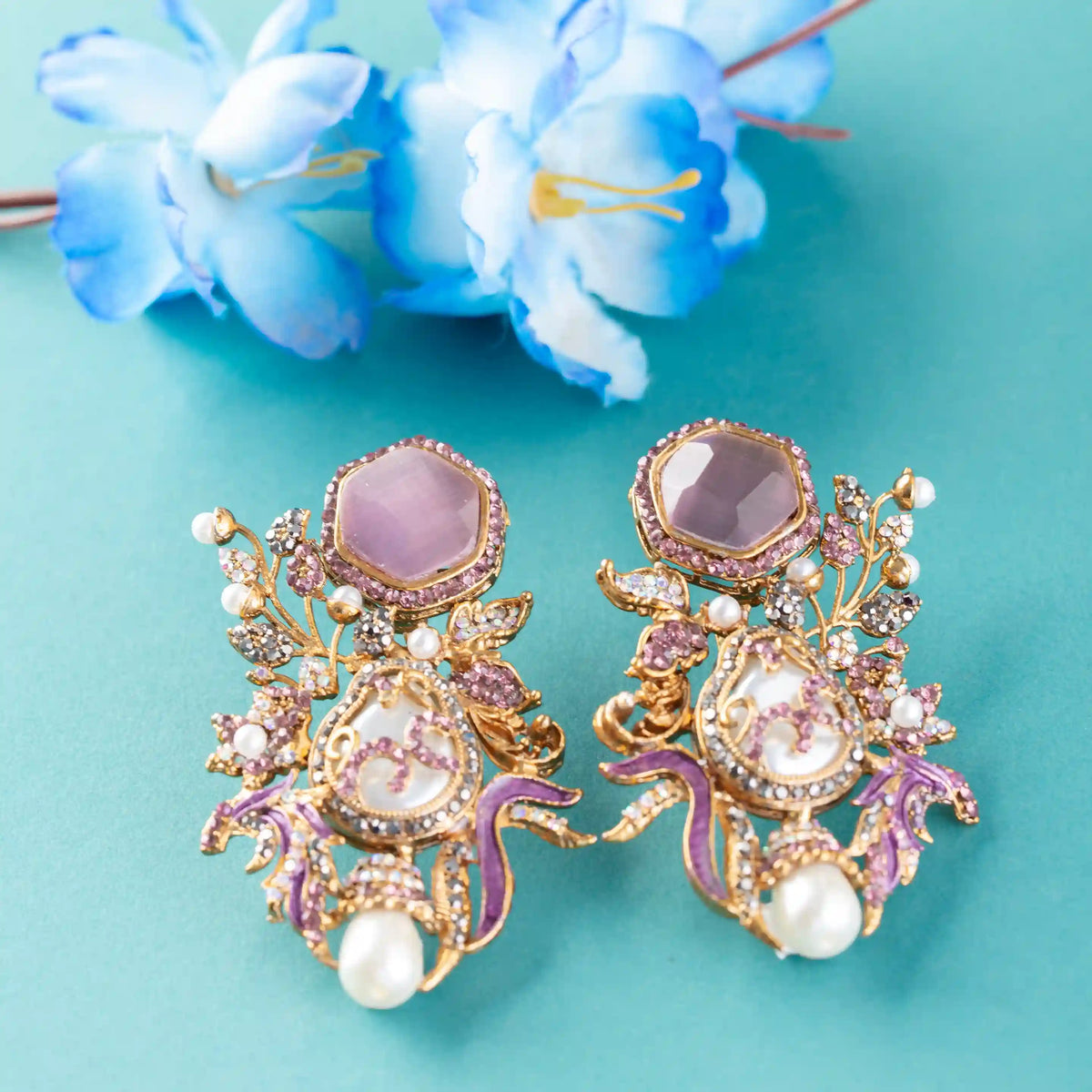 Ornate earrings with purple and gold colors on a teal background