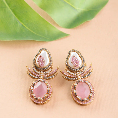 Ornate earrings with pink stones on a beige surface with green leaves.