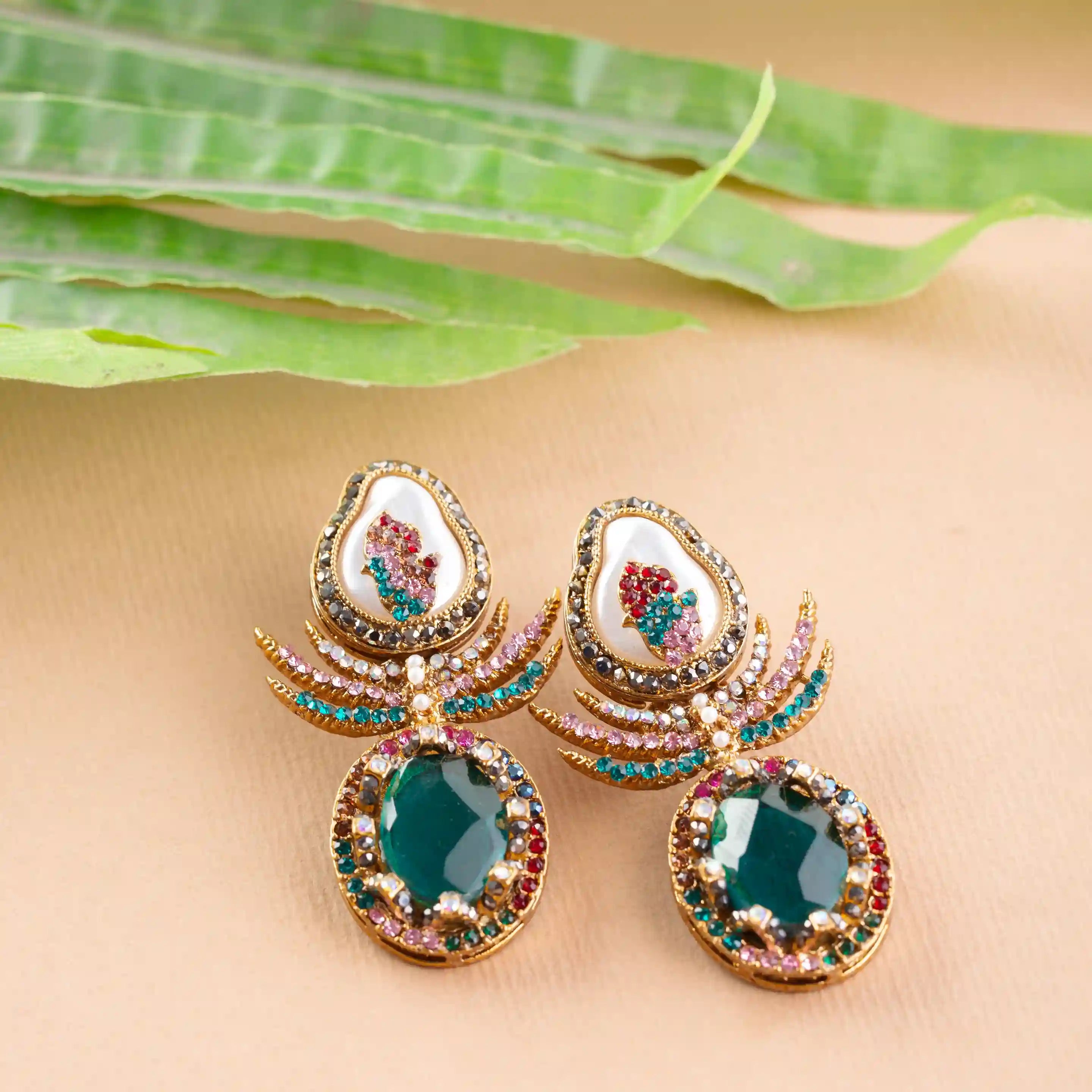 Ornate earrings with gemstones on a beige surface with green leaves.