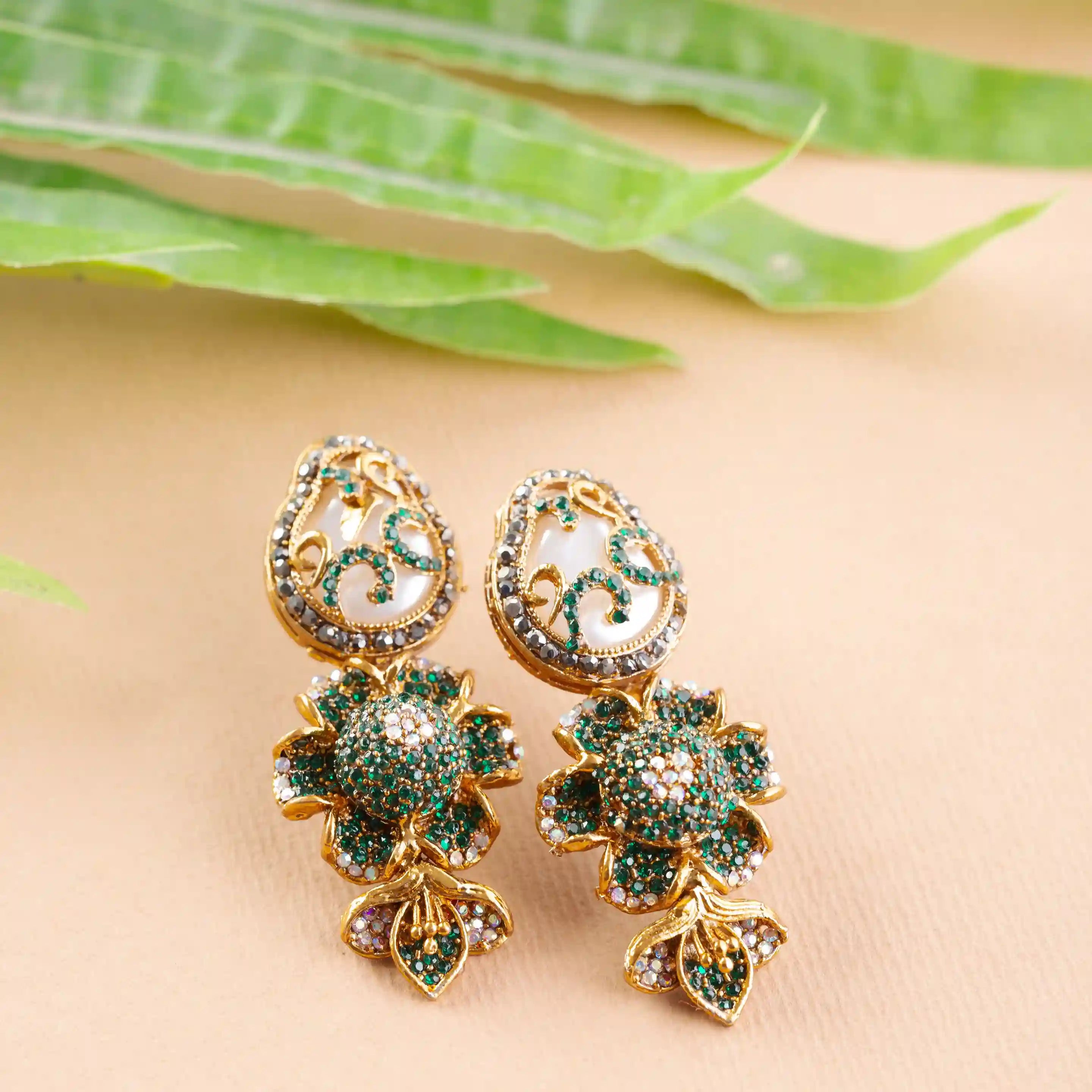 Gold and green earrings on a beige surface
