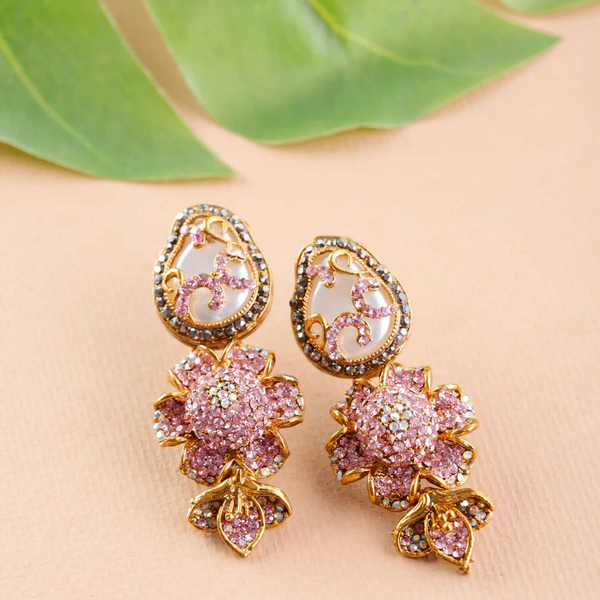 Pair of ornate earrings with pink floral designs on a beige surface
