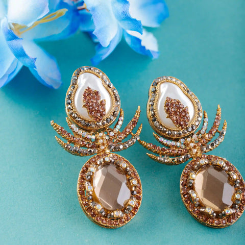 Pair of ornate earrings with gold and brown details on a teal background