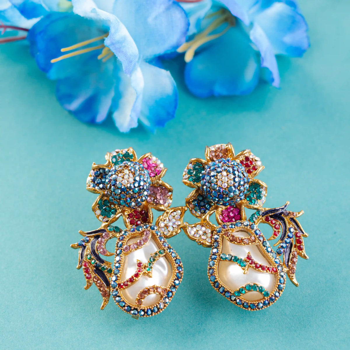Colorful floral earrings on a turquoise background with blue flowers.
