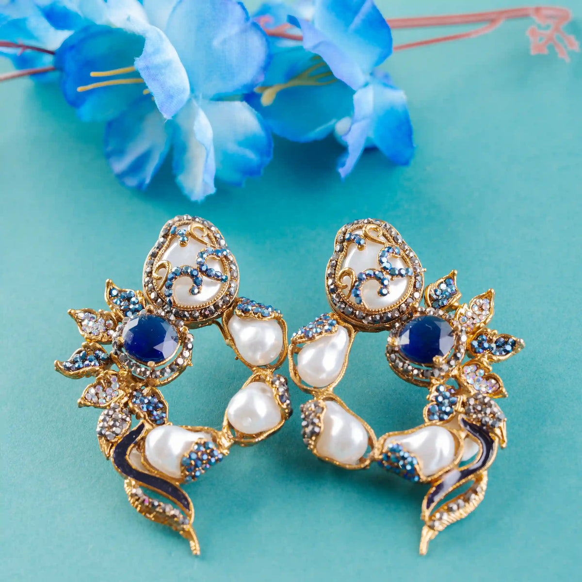 Pair of ornate earrings with pearls and blue stones on a turquoise background