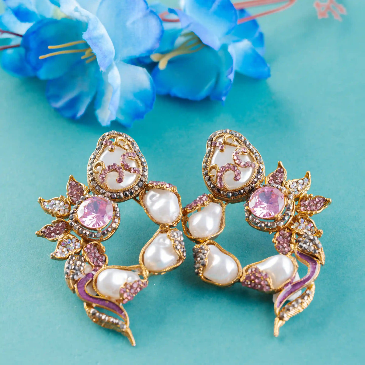 Pair of ornate earrings with pink and white stones on a teal background