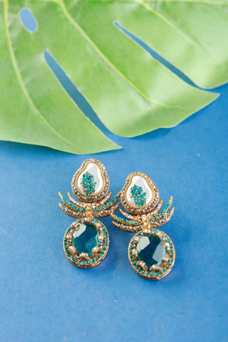 Gold and green earrings on a blue surface