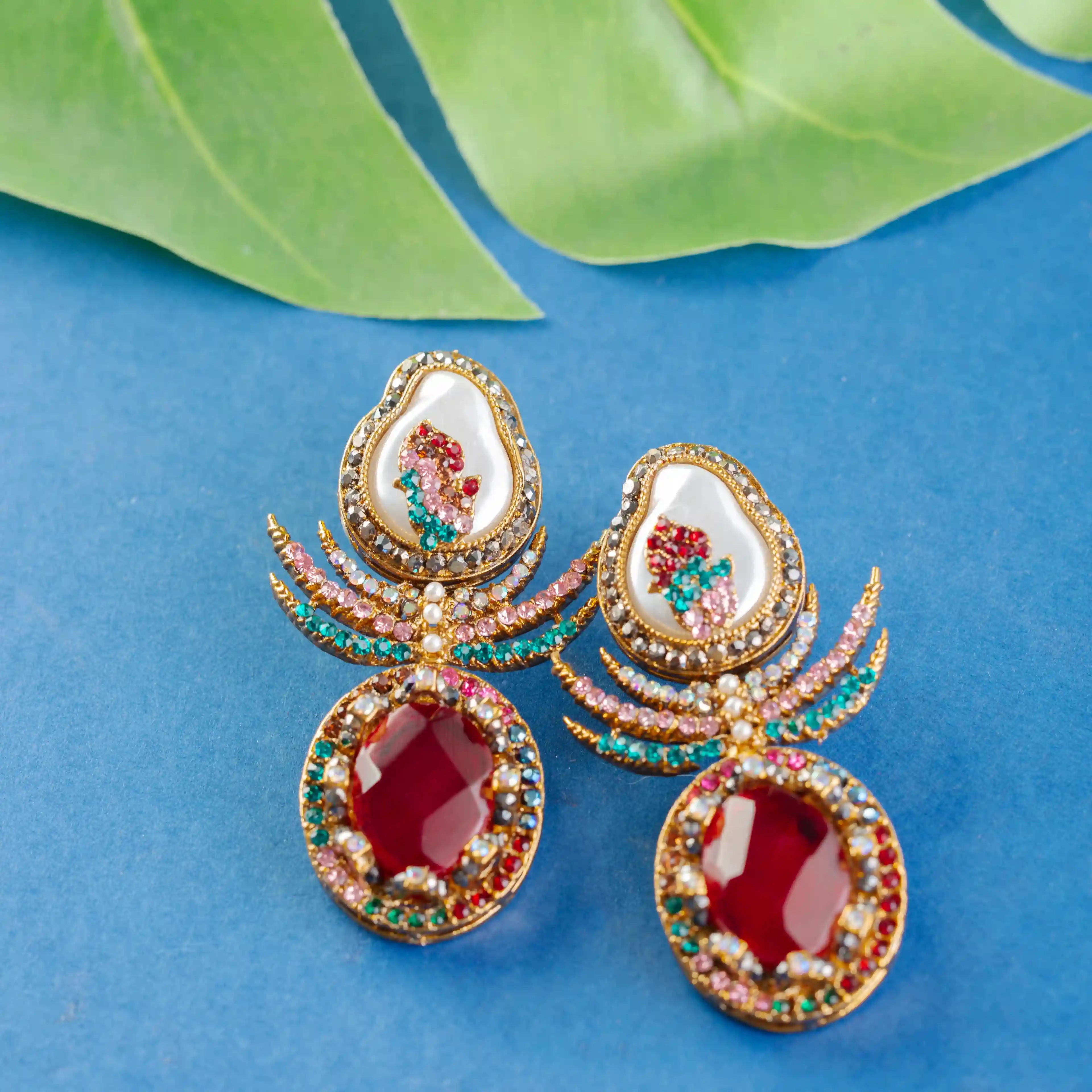 Ornate earrings with red stones and gold detailing on a blue background