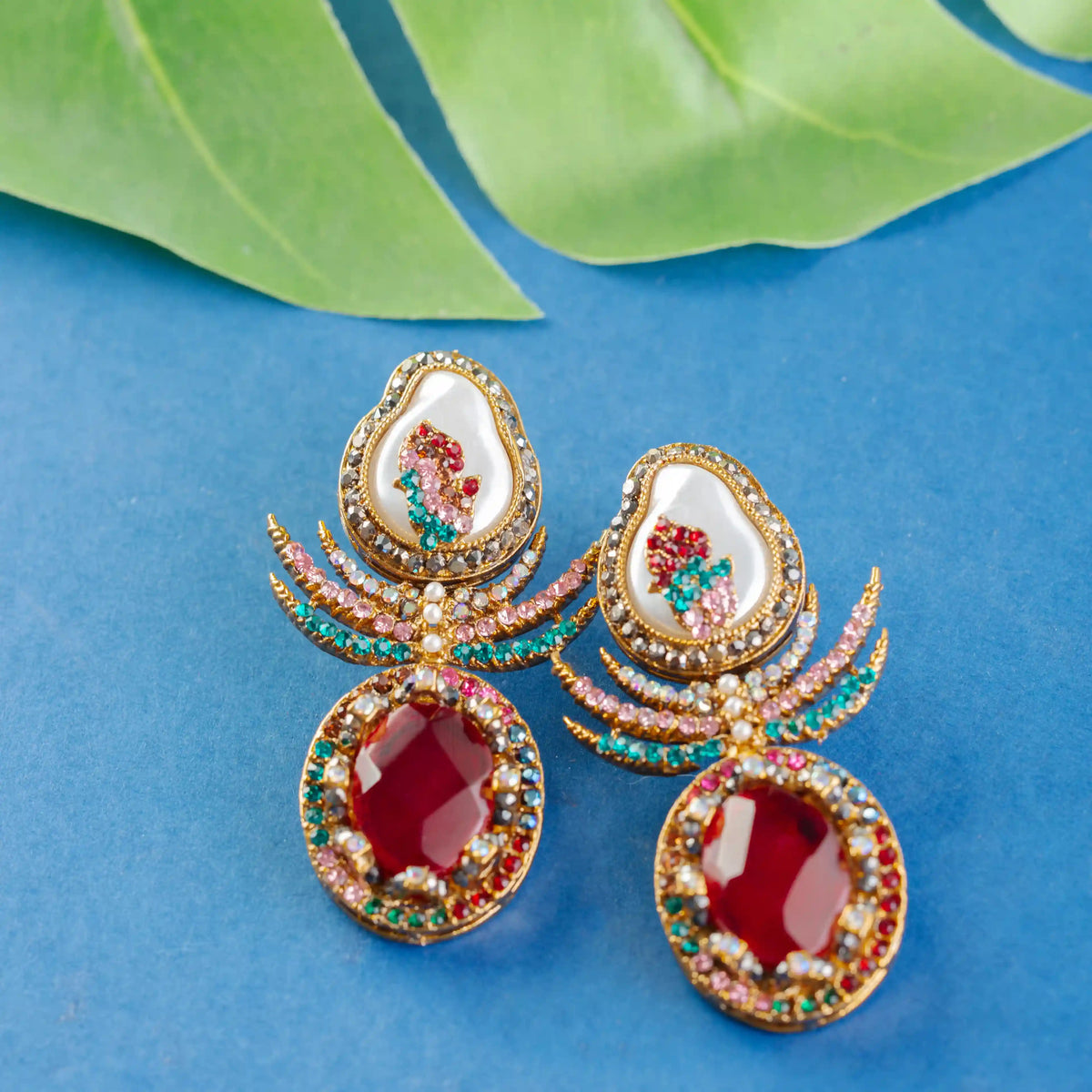 Ornate earrings with red stones and gold detailing on a blue background