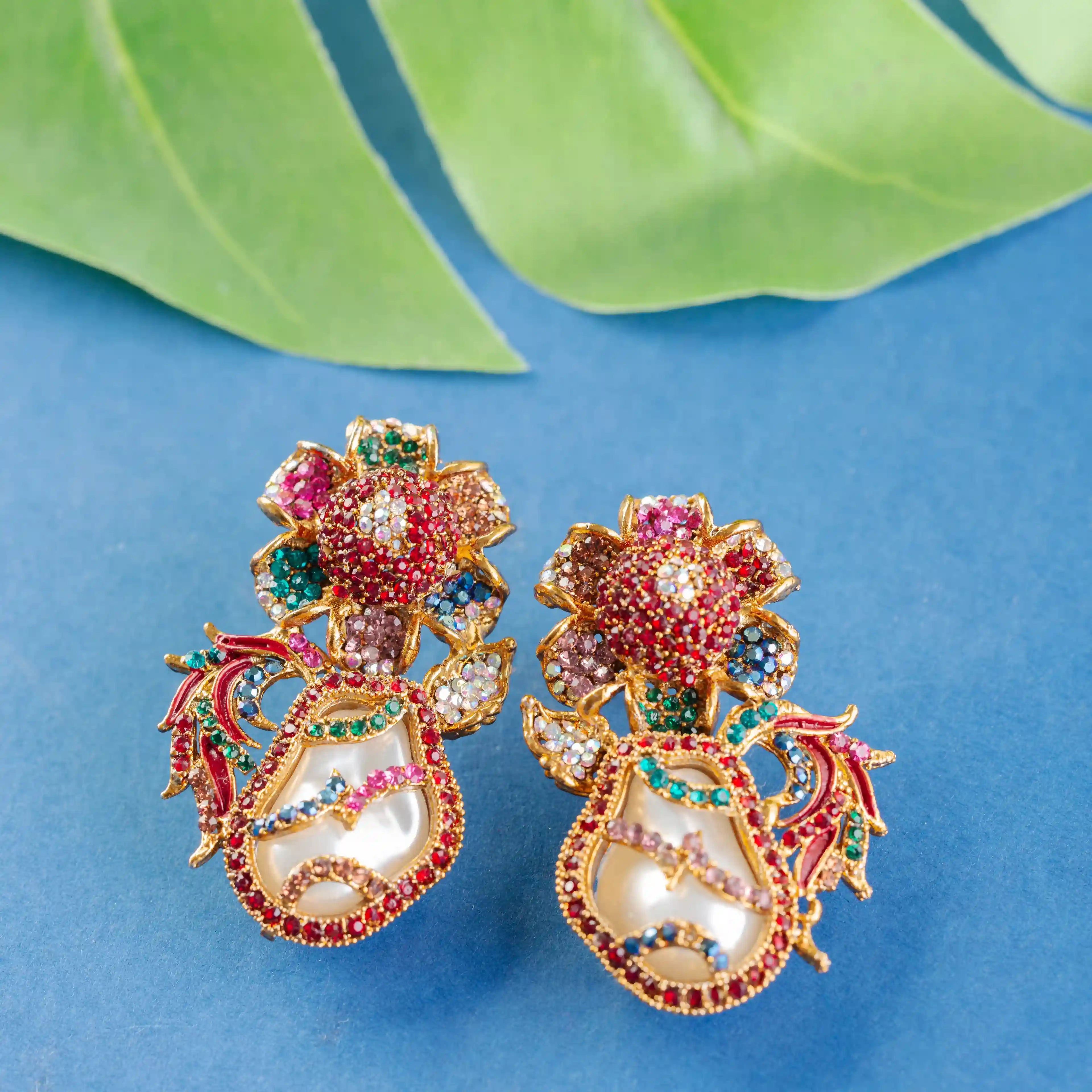 Colorful floral earrings on a blue background with green leaves
