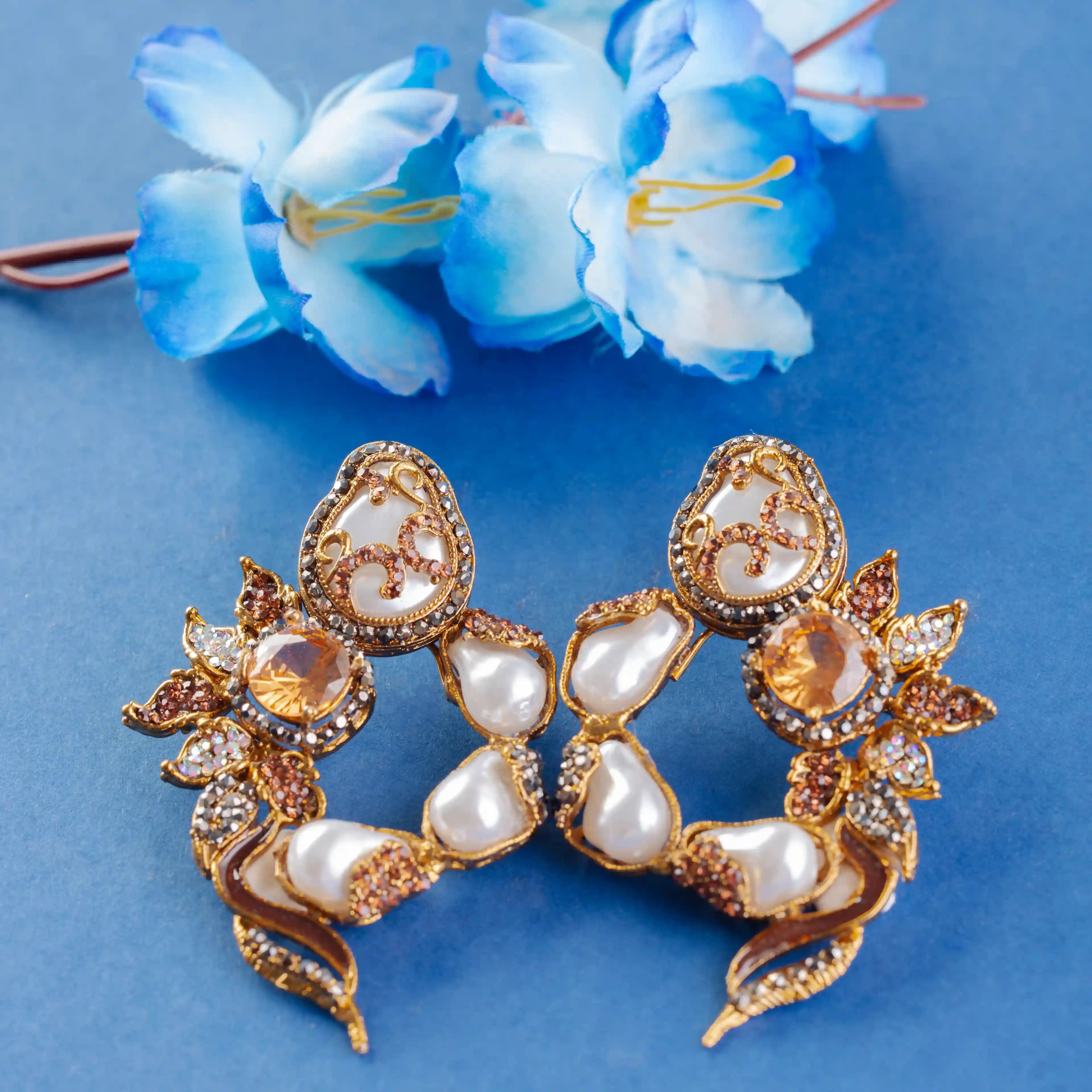 Gold and pearl earrings on a blue background with blue flowers.