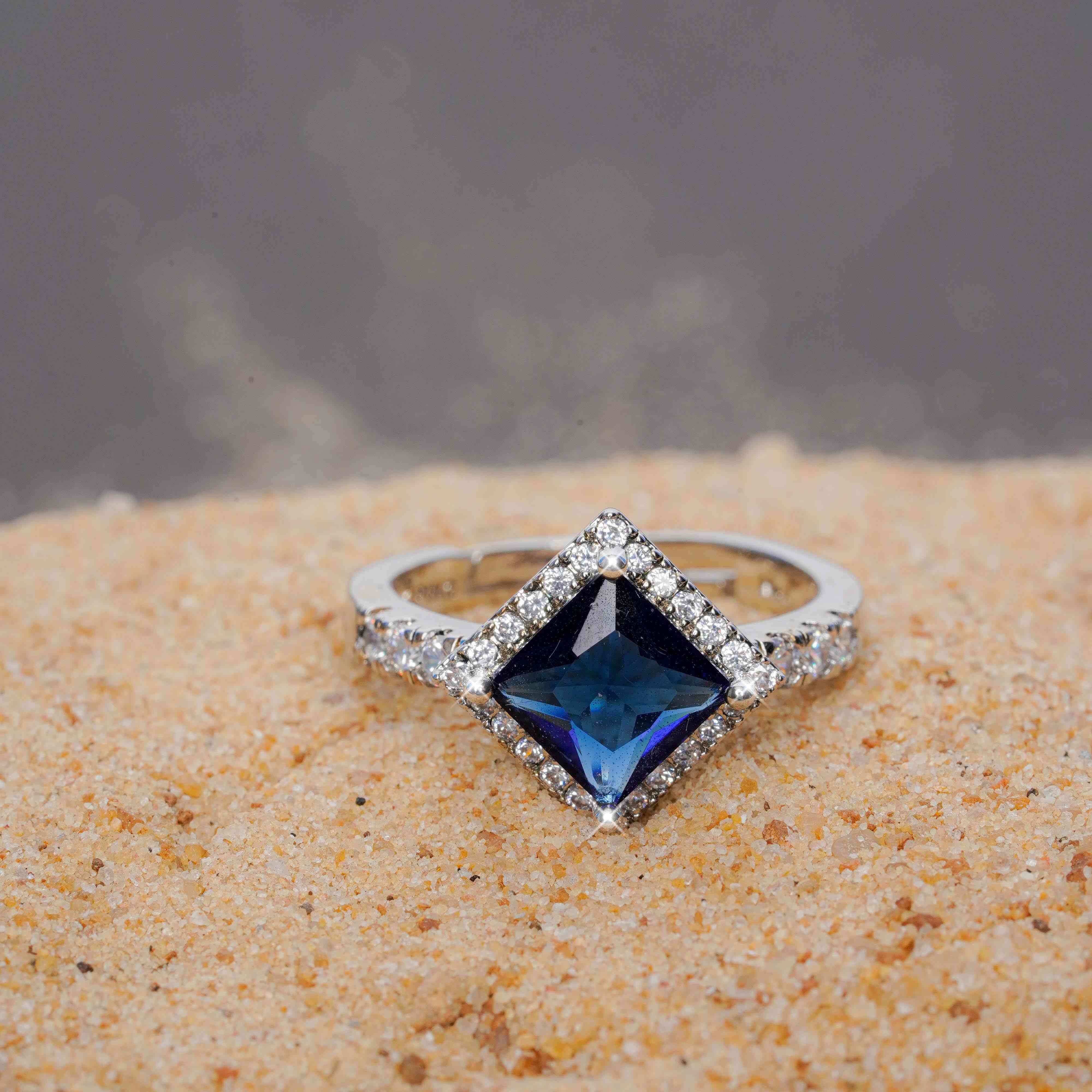 Silver ring with a blue gemstone on a sandy surface