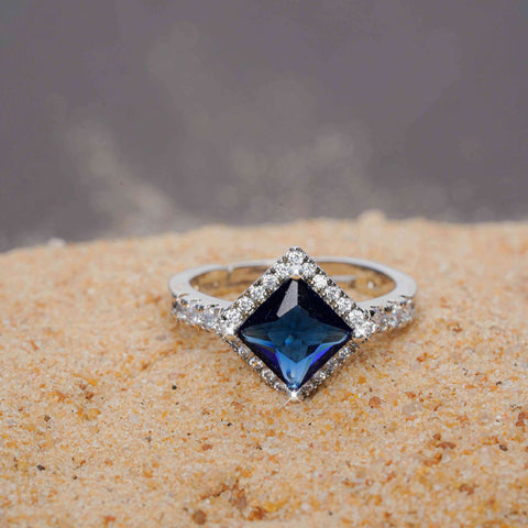 Silver ring with a blue gemstone on a sandy surface