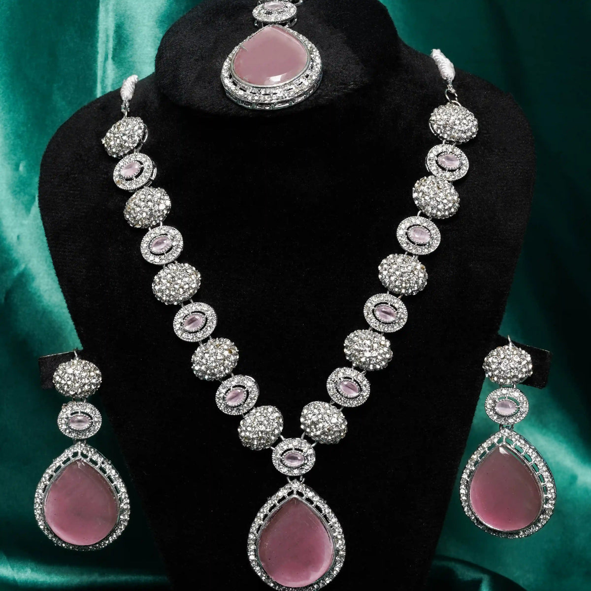Jewelry set with pink stones and silver accents on a black stand against a green background