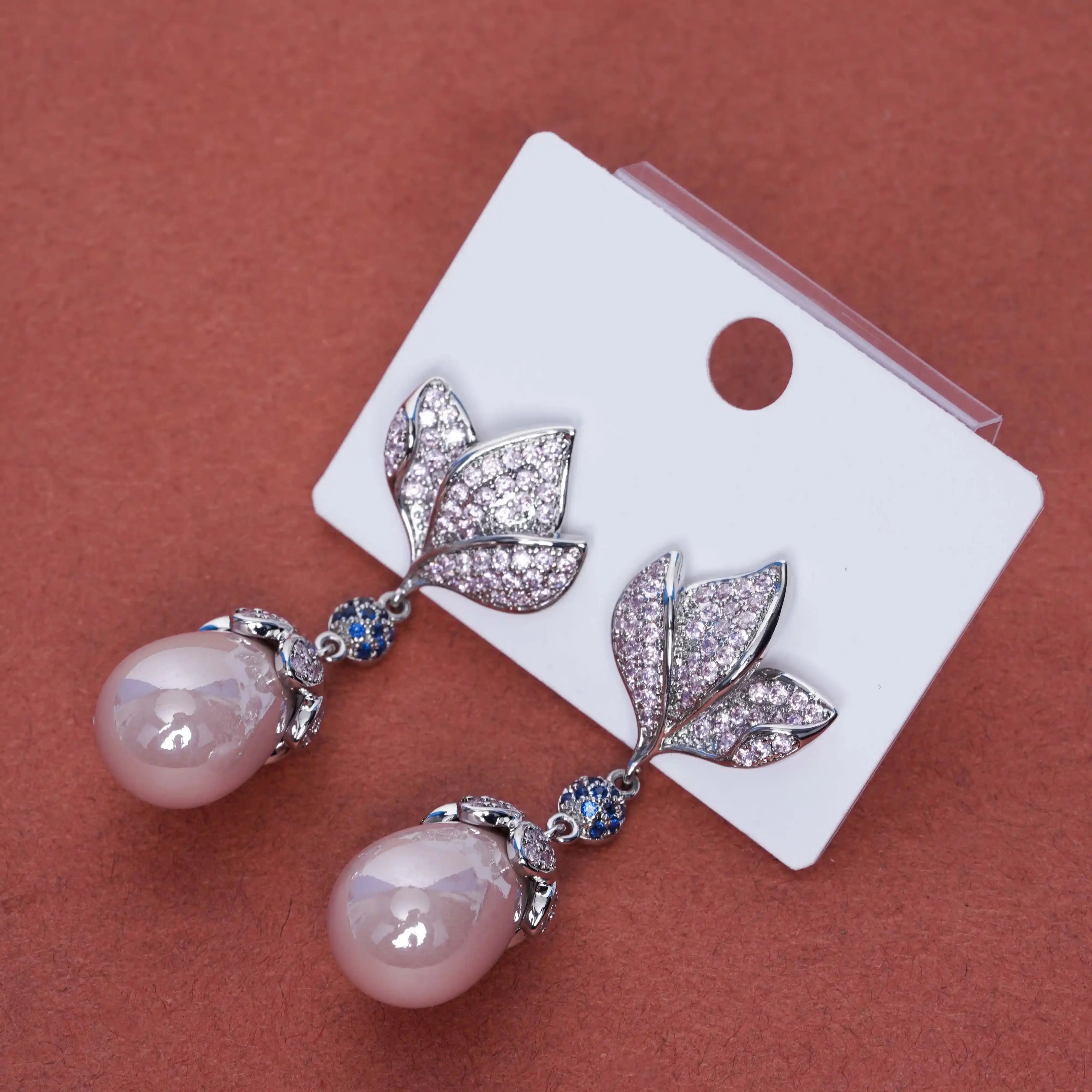 Pair of earrings with pink beads and leaf-like designs on a white card against a brown background