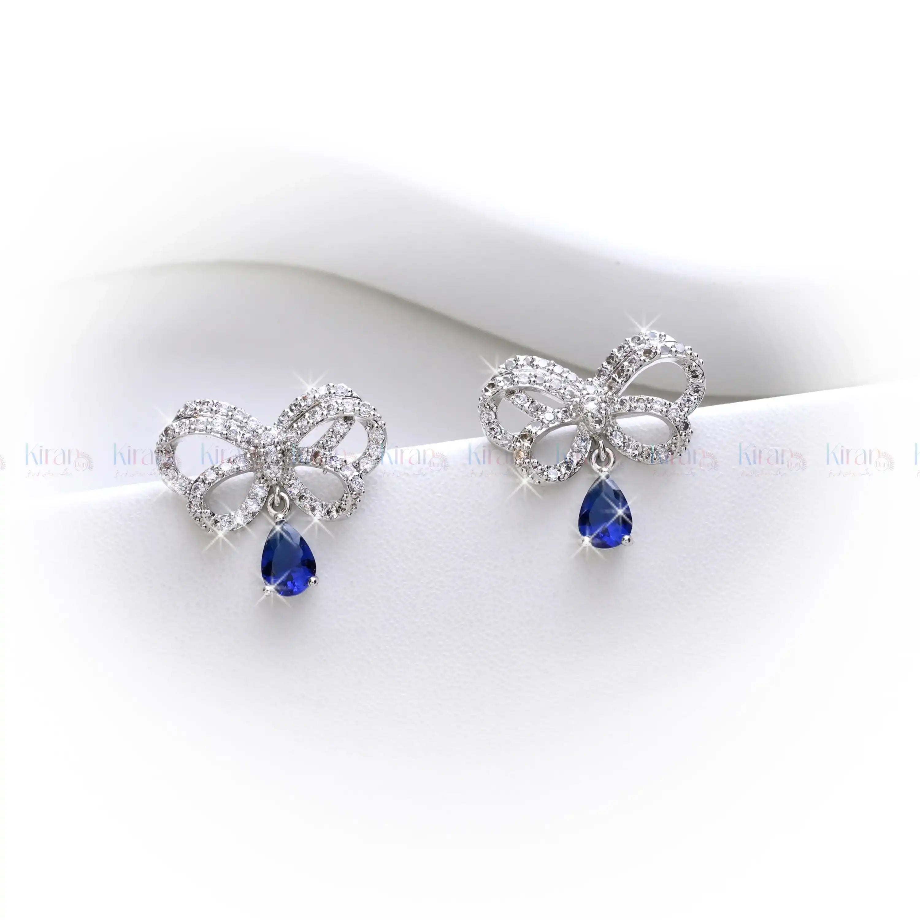 Bow-shaped earrings with blue teardrop stones on a white background