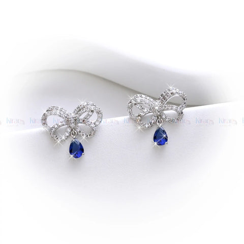 Bow-shaped earrings with blue teardrop stones on a white background