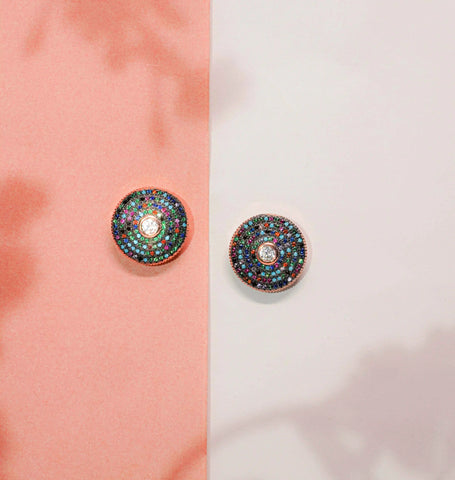 Pair of round earrings with colorful gemstones on a pink and white background