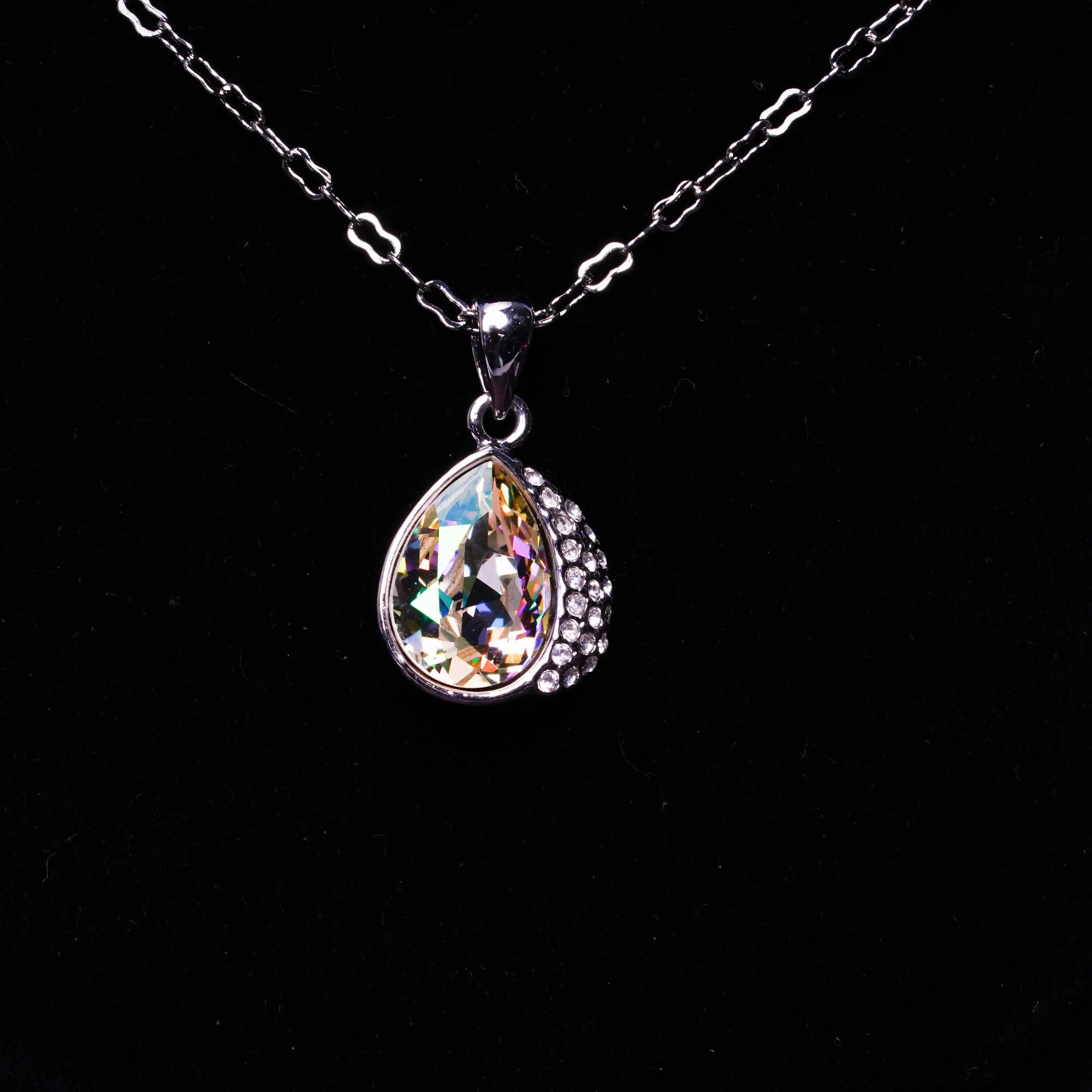 Teardrop-shaped crystal pendant on a chain against a black background