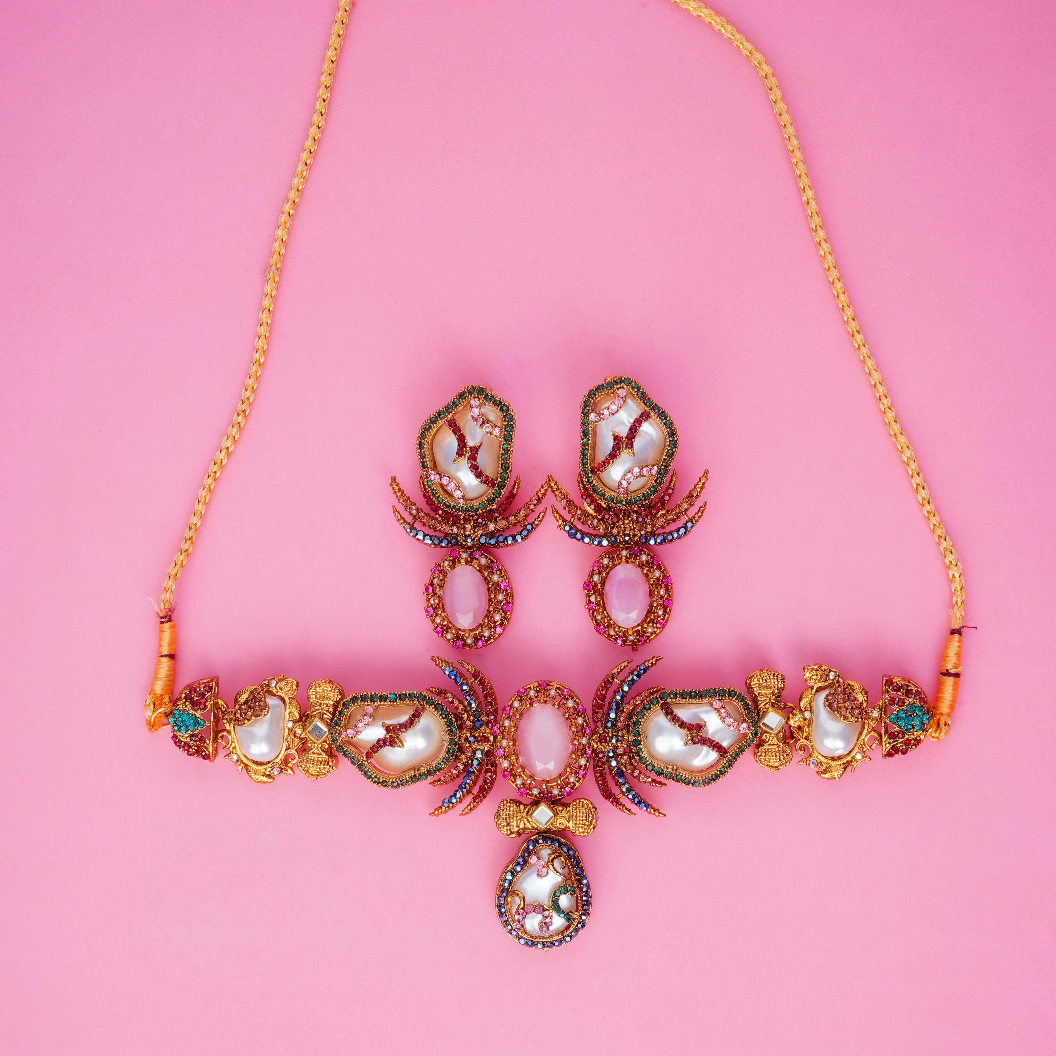 Ornate necklace and earrings on a pink background