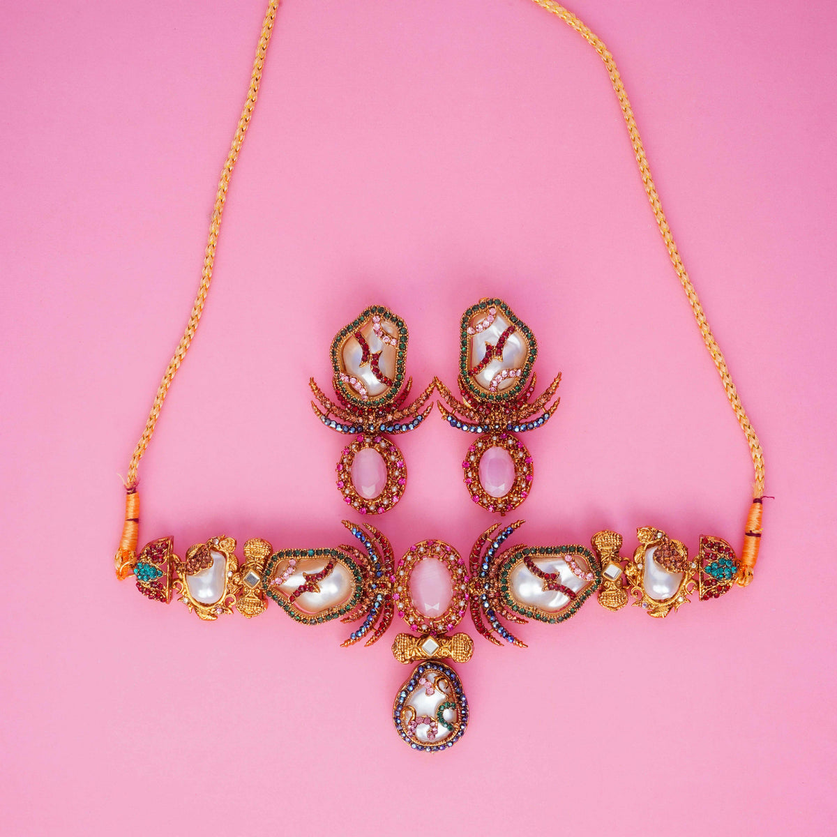 Ornate necklace and earrings on a pink background