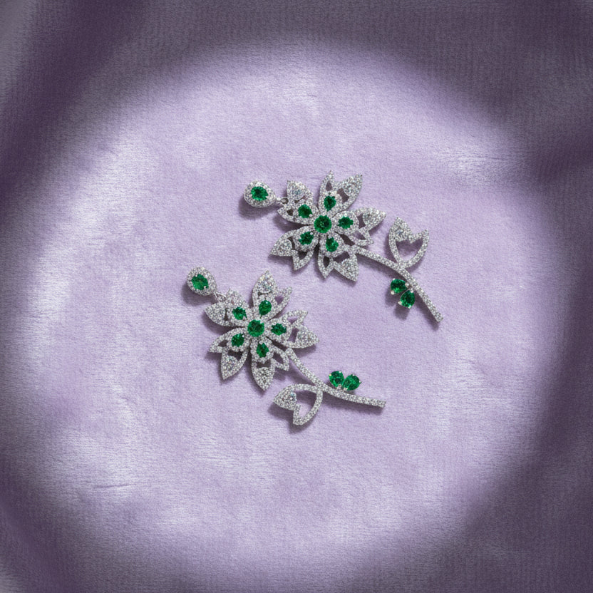 Pair of floral earrings with green gemstones on a white cushion