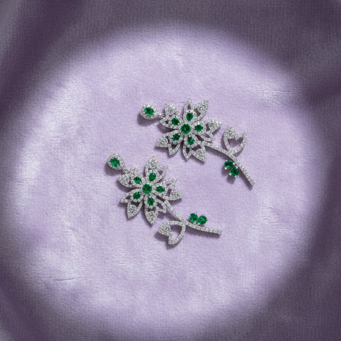 Pair of floral earrings with green gemstones on a white cushion