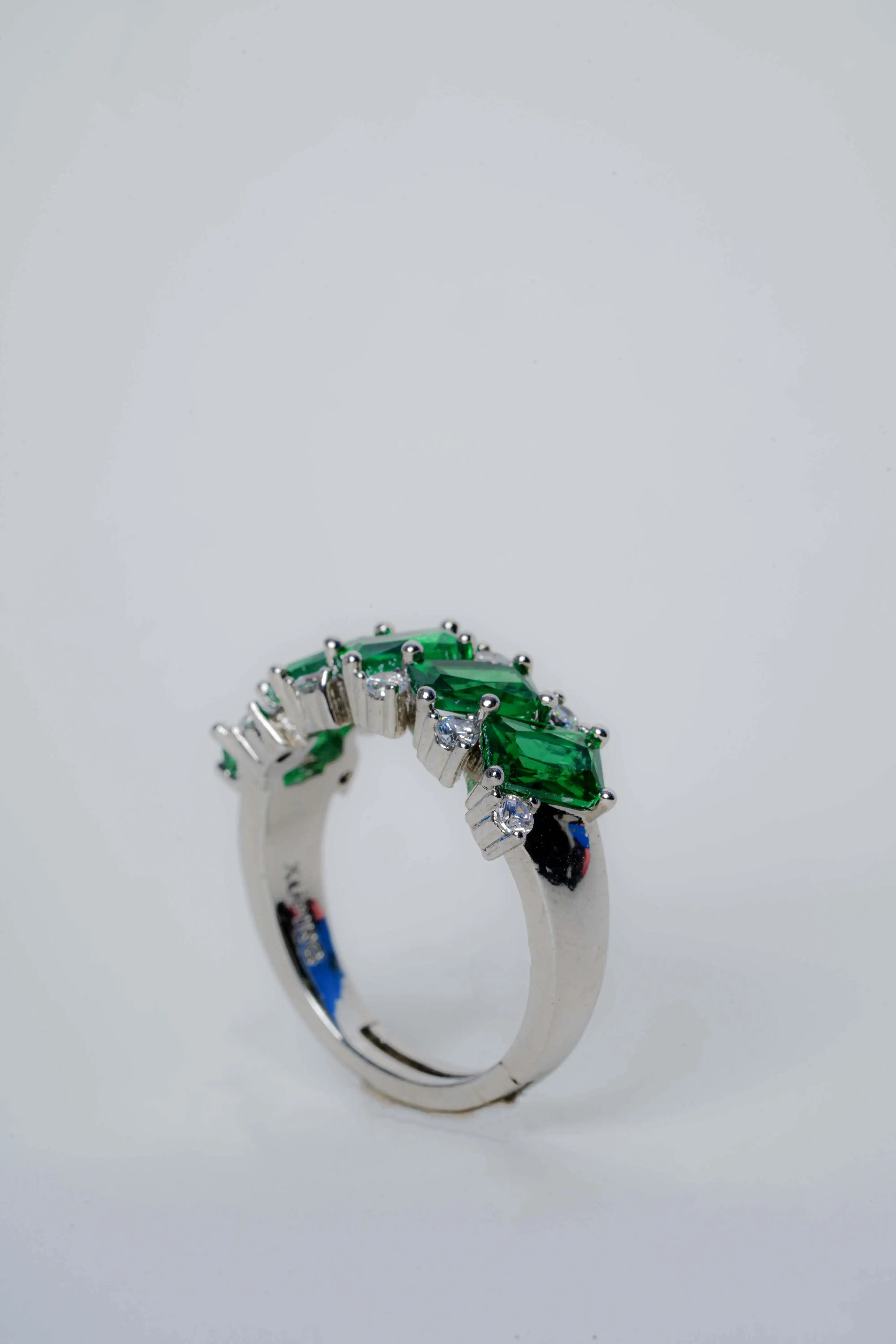 Silver ring with green gemstones on a light gray background
