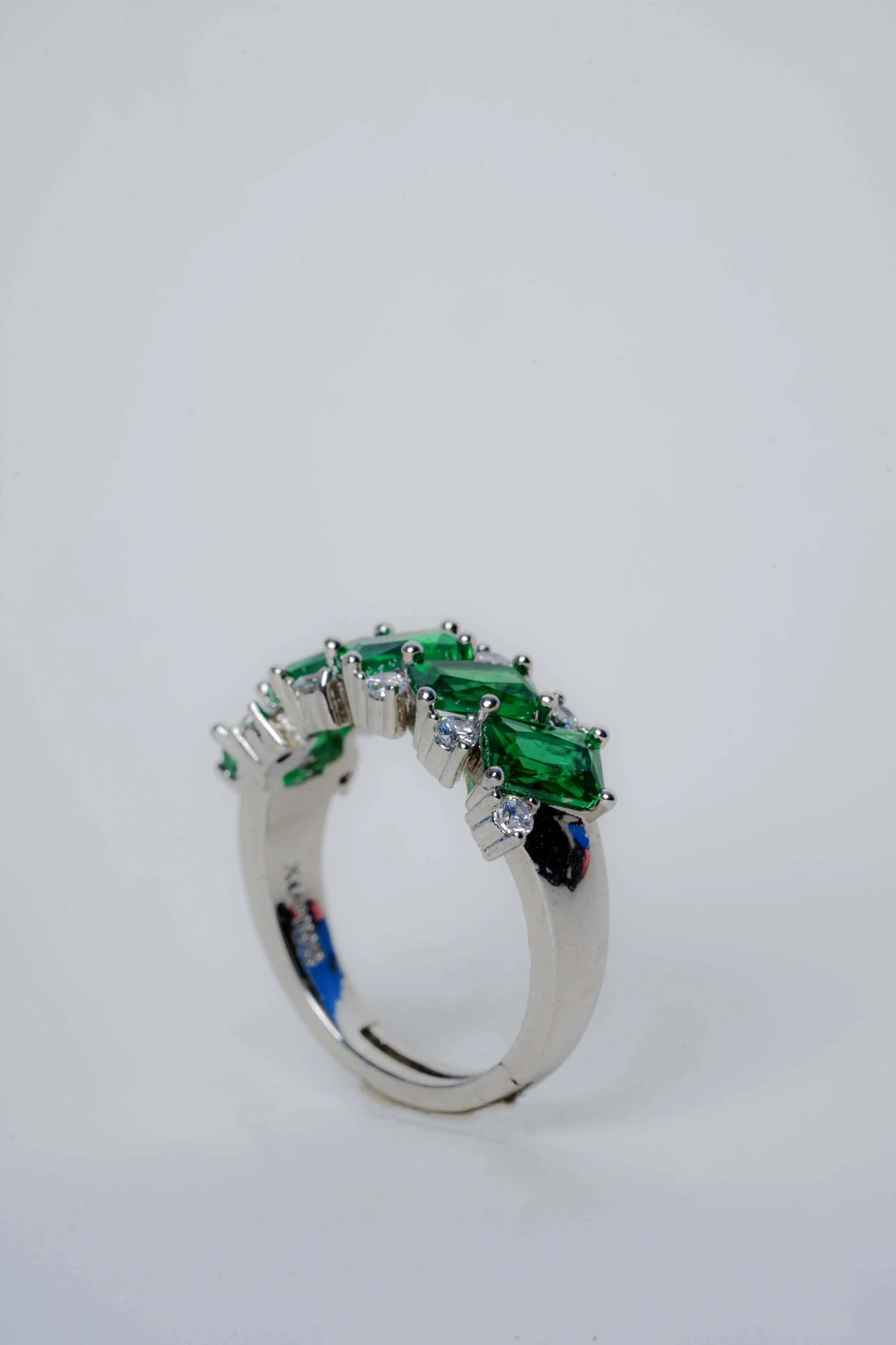 Silver ring with green gemstones on a light gray background