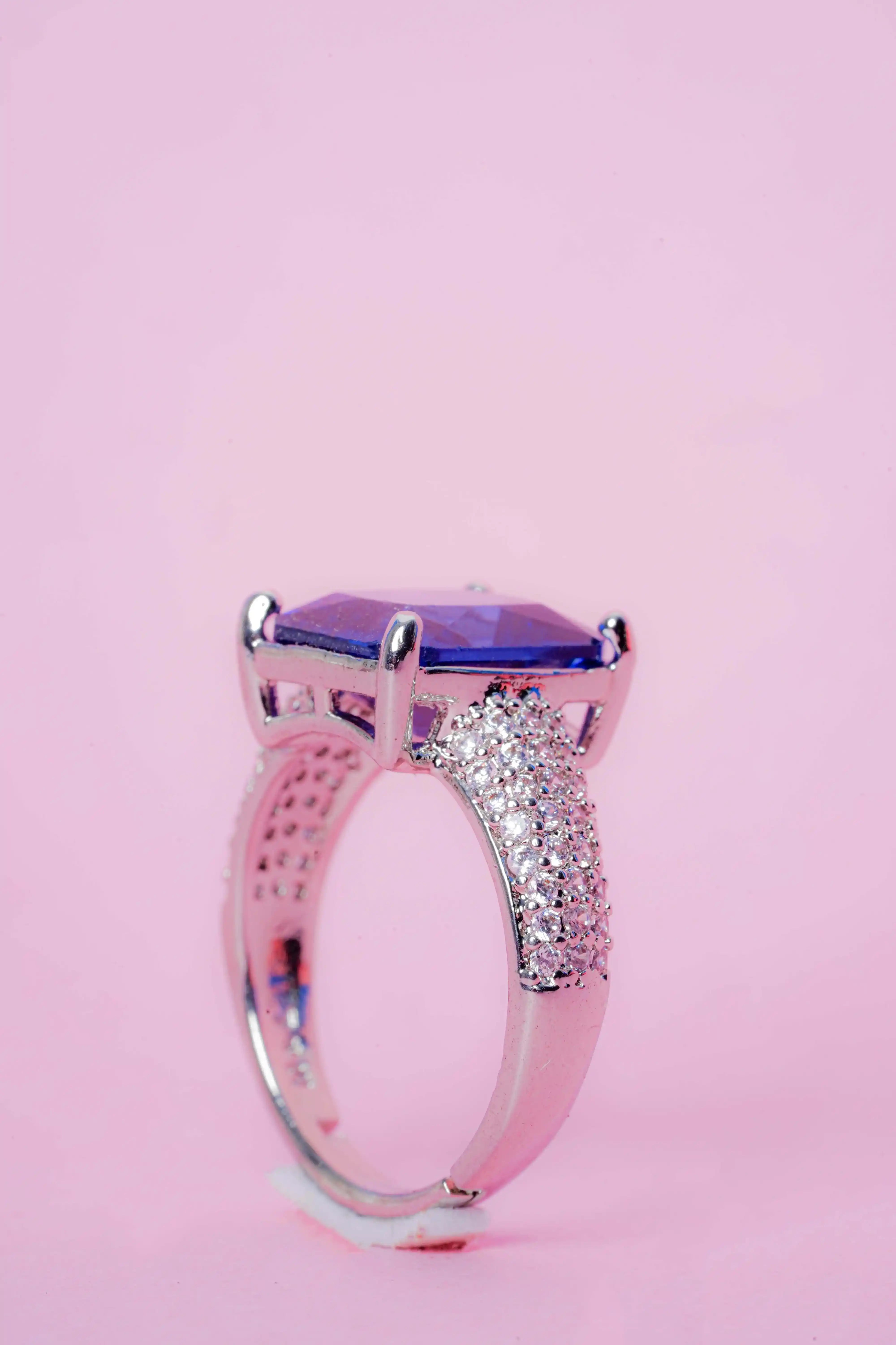 Ring with a purple gemstone and diamond-studded band on a pink background