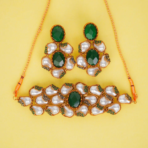 Ornate necklace and earrings set with green and pearl-like stones on a yellow background