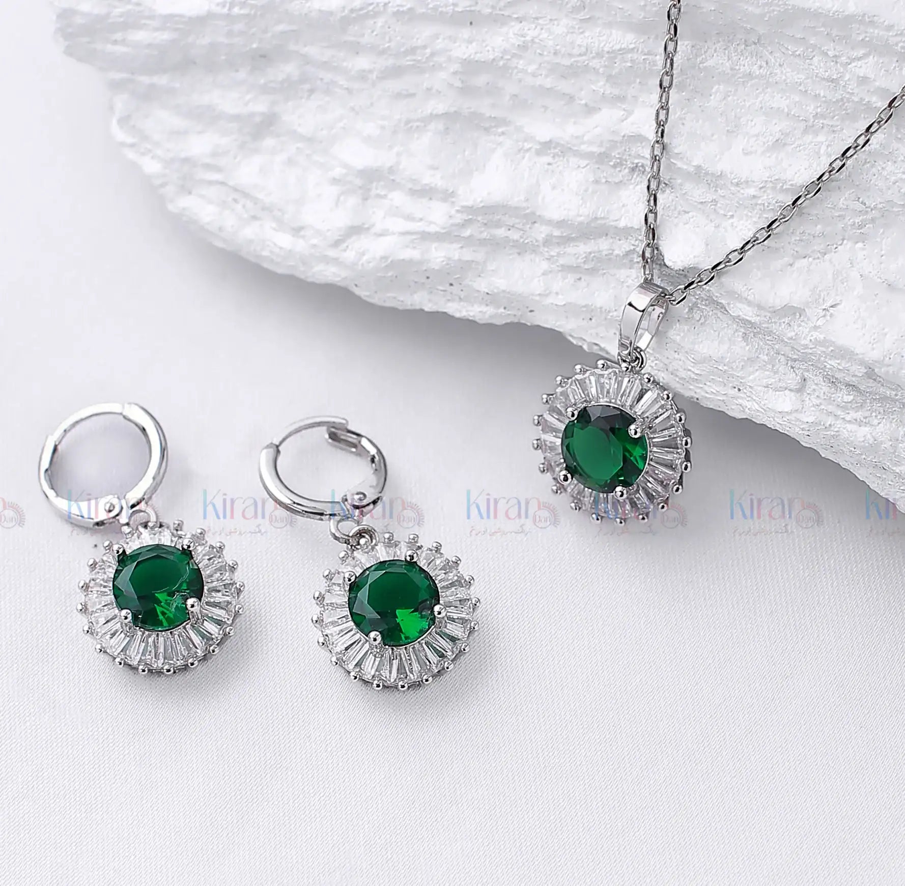 Silver jewelry set with green gemstones on a white background