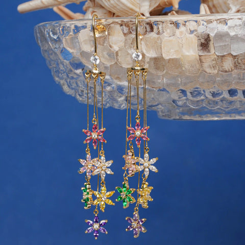 Colorful flower-shaped earrings on a clear stand against a blue background