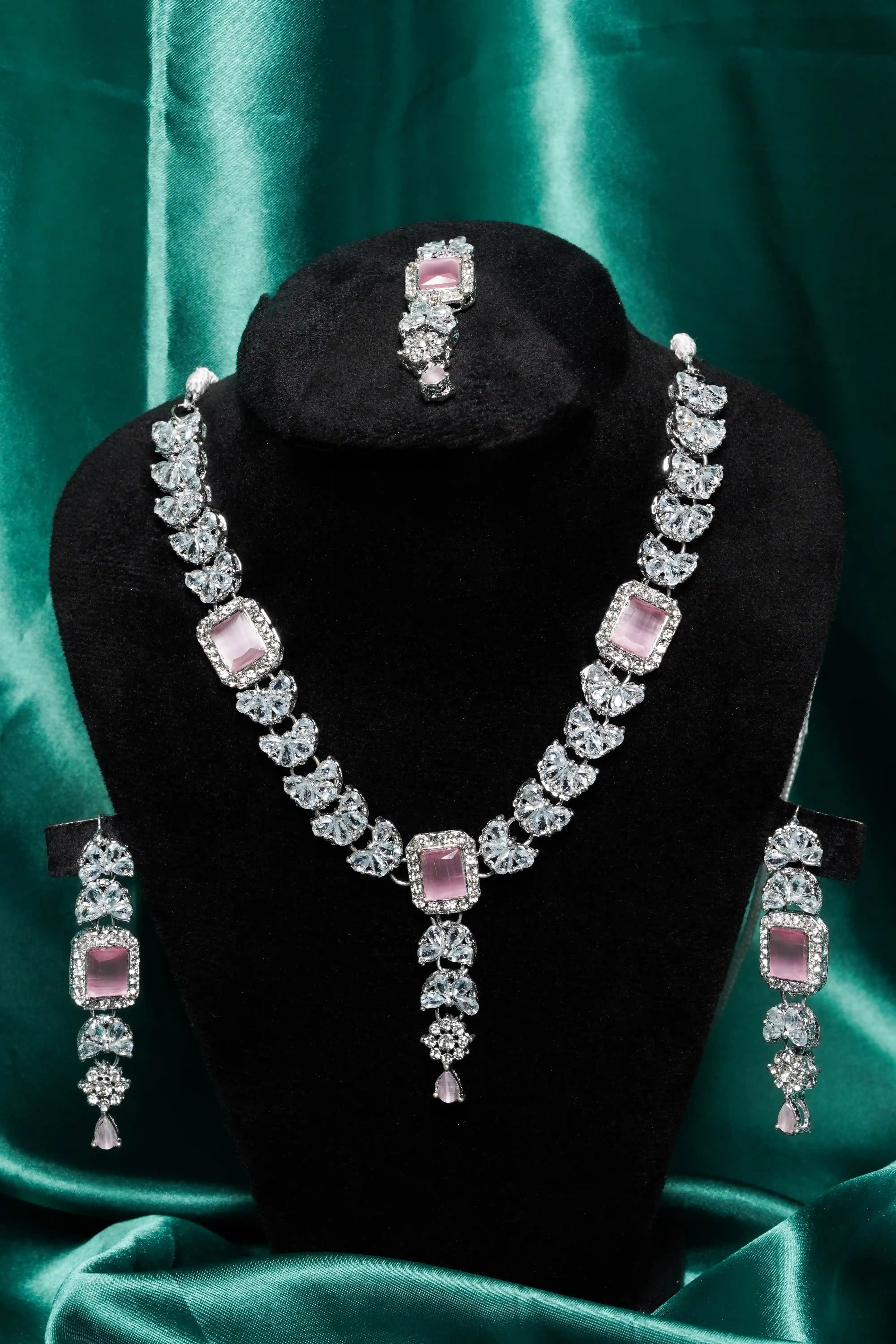 Jewelry set with necklace and earrings on a black stand against a green satin background