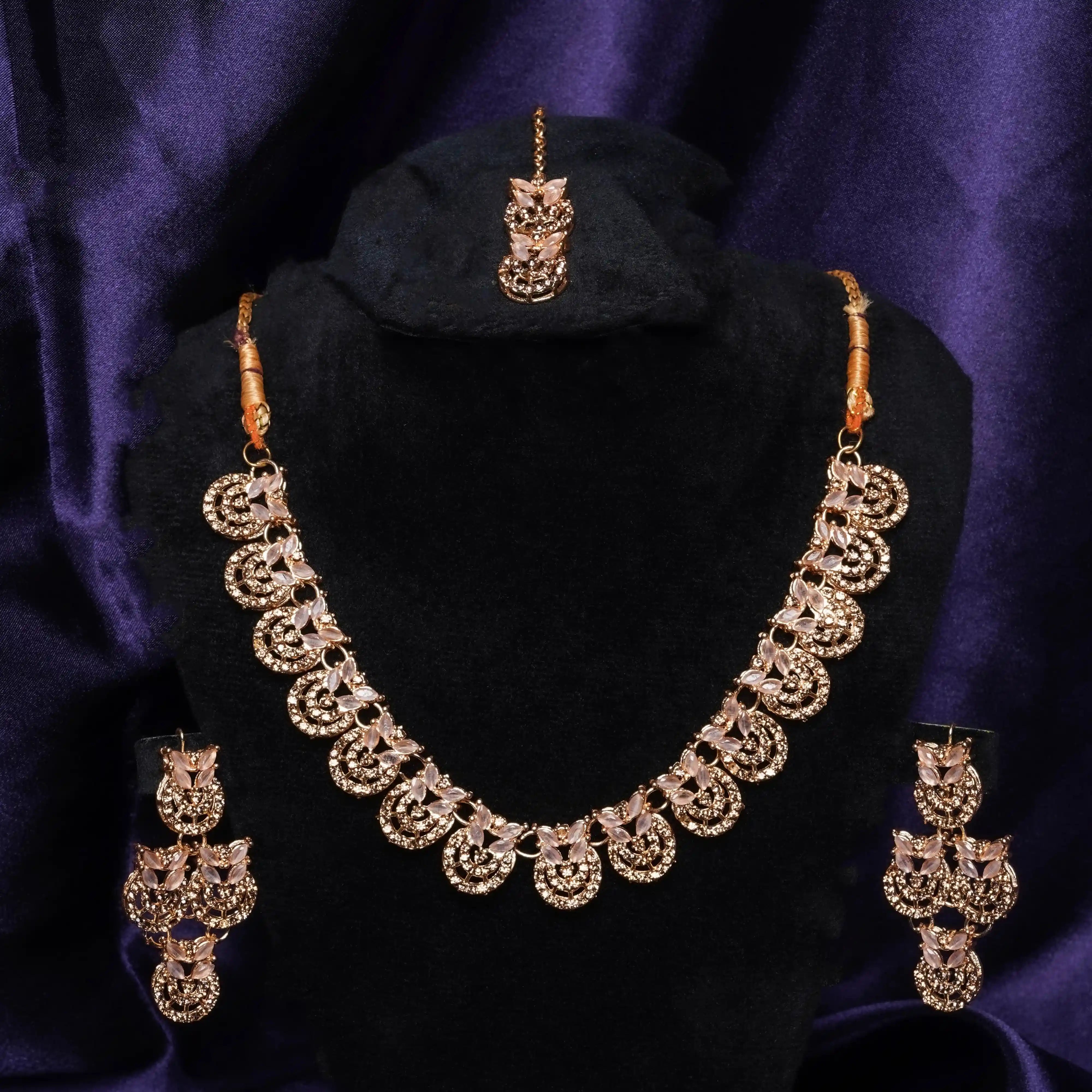 Gold necklace set with matching earrings on a black stand against a purple background