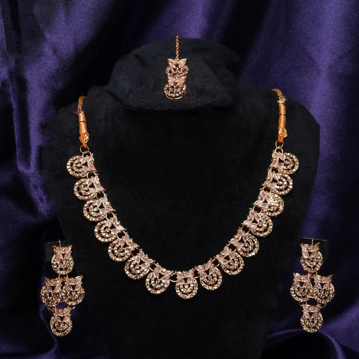 Gold necklace set with matching earrings on a black stand against a purple background