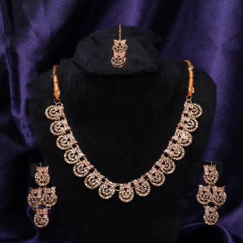 Gold necklace set with matching earrings on a black stand against a purple background