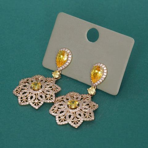 Gold earrings with yellow gemstones on a gray card against a teal background