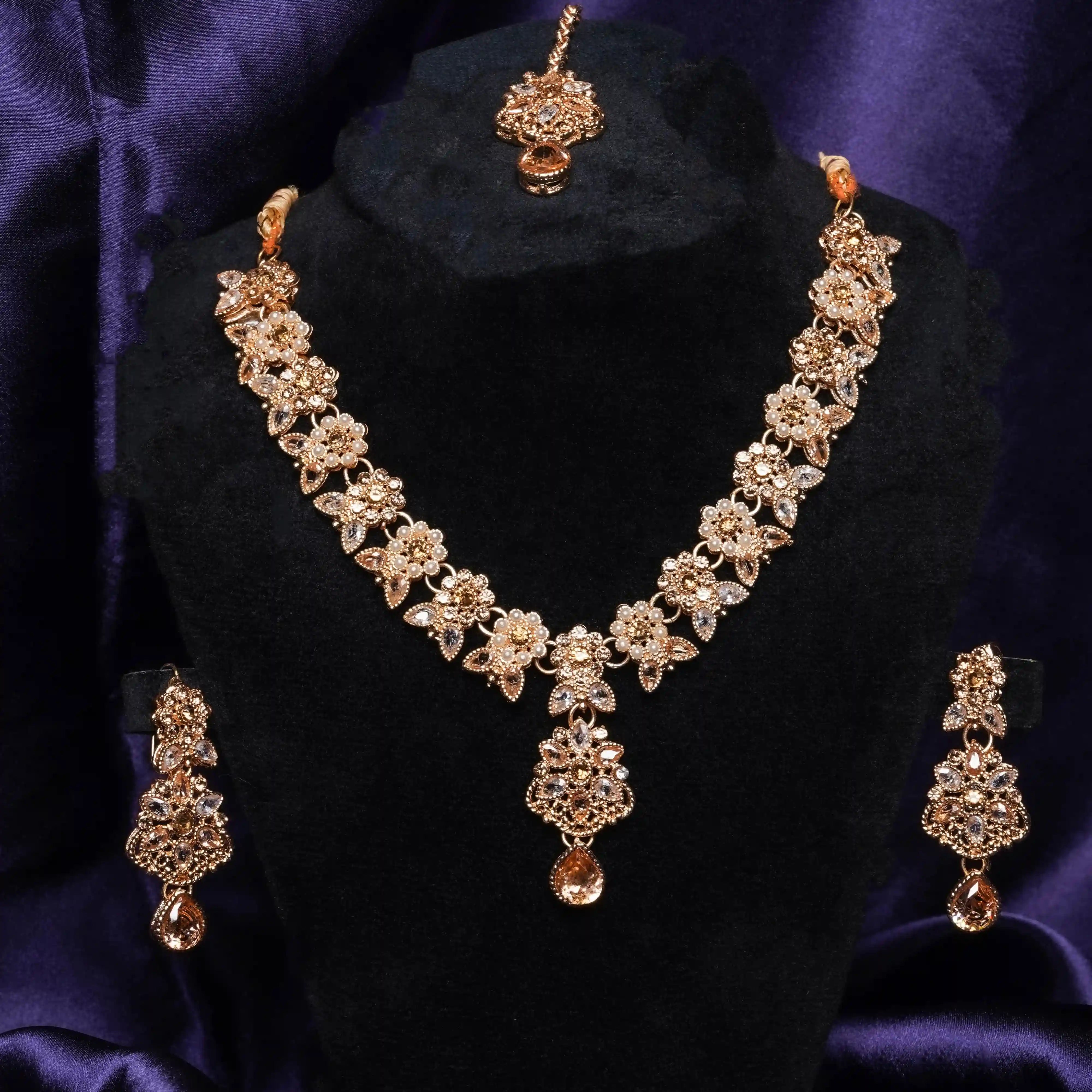Gold necklace and earrings set on a black stand with purple background